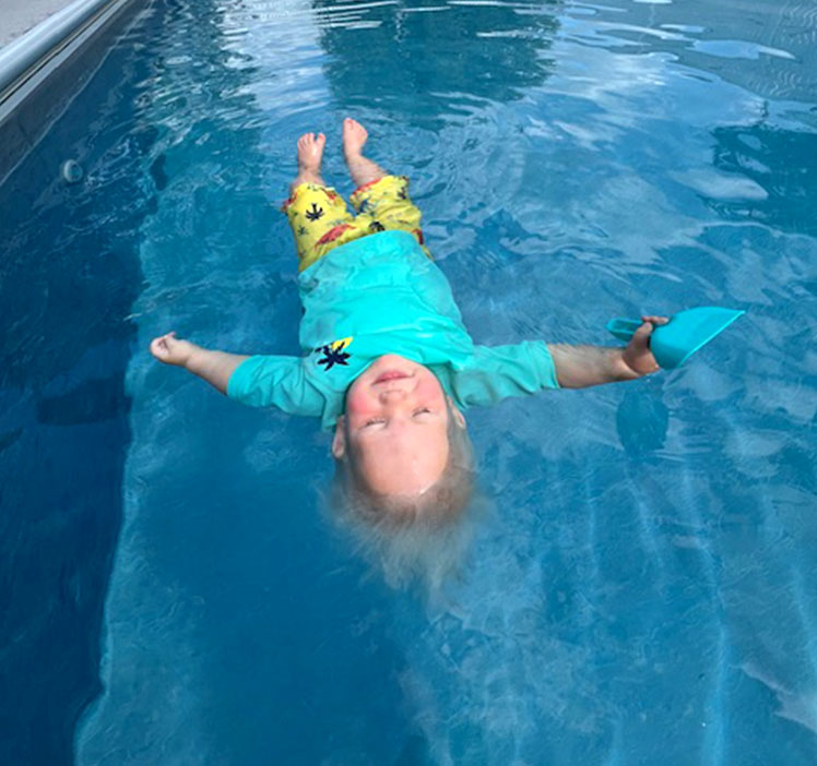 Young swimmer floating while holding a toy